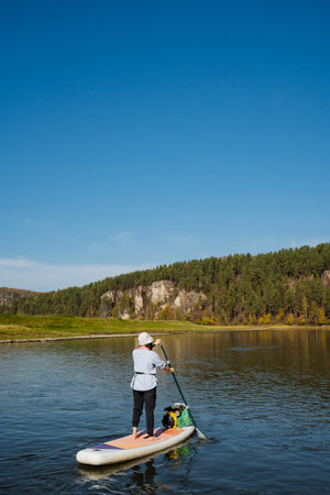 A person is paddleboarding on a calm lake, surrounded by lush forests and a clear blue sky, creating...
