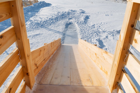 Wooden Slide Entrance To Snow Track Showing Timber Steps And Ramp Leading Into Fresh Powder, Visible Footprints And Bright Winter Light, Close Viewpoint Evoking Play, Anticipation And Outdoor Familyの写真素材