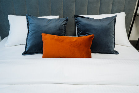 White Bed Layered With Orange Cushion, Soft Navy Pillows Against Gray Upholstered Headboard, Crisp White Linens, Hotel Style Staging For Boutique Living, Minimalist Modern Vibe, Inviting Cozyの写真素材