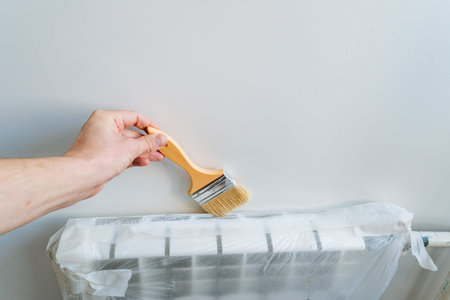 Painting Radiator With Protective Cover, Closeup Of Bristles Applying White Paint Carefully, Meticulous Artist Applying White Paint To Radiator Fins With Protective Plastic Surroundingの写真素材