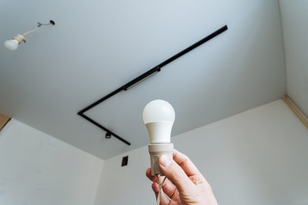 Hand Inspecting LED Bulb And Loose Ceiling Wire In Staged Renovation, Technician Assessing Socket...