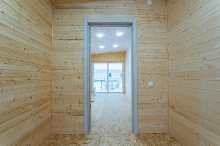 View Through Doorway Into Adjacent Pine Room Showing Threshold, Recessed Ceiling Lights And Unfinished Floor, Architectural Perspective Highlighting Transition Between Interior Spaces In New Buildの写真素材