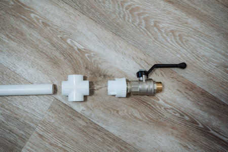 Disassembled Valve And Pvc Fittings Laid On Wood Floor For Inspection By Service Technician, Cross Fitting And Union Displayed Next To Brass Ball Valve Showing Threads And Seals, Organized Layoutの写真素材