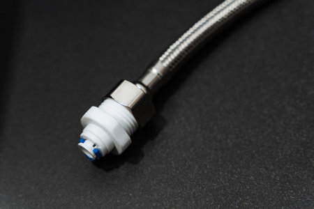 Metal Braided Hose Connector On Black Background, Closeup Of Stainless Braided Hose With Plastic Push Fit End, Studio Lighting Emphasizes Texture, Threads And Sealing Surfaces, Useful For Plumbingの写真素材
