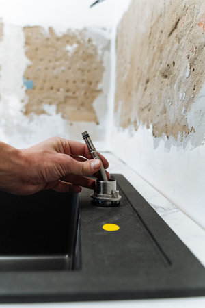 Close Up Hand Tightening Sink Mounting With Screwdriver On Black Sink, Renovator Aligning Hole For New Fixture, Exposed Backsplash And Worktop Preparation, Dust And Adhesive Remnants, Carefulの写真素材