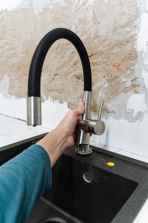 Aligning Plumbing Fixture Over Kitchen Basin. Adjusting Black Kitchen Faucet During Installation Process Testing Flow. Closeup Of Hand Aligning And Testing Flow Of Countertop Mounted Kitchen Faucetの写真素材