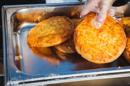 Gloved Hand Lifting Warm Pastry At Market. Outdoor Food Vendor Presenting Golden Bakery Treats...