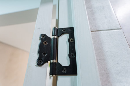 Detailed view of a sturdy metal hinge fastened with screws on a glass panel door frame, showing clean industrial hardware, smooth surfaces, and neutral indoor lighting