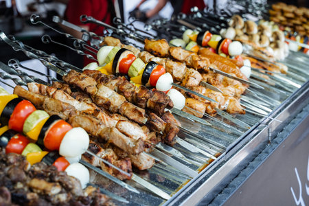 Close-up view of multiple skewers arranged in rows on a metal grill display at a street food market. The skewers hold charred pieces of marinated meat, whole boiled eggs, bell