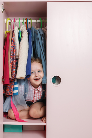 A little girl is sitting in a wardrobe with a children's department. Storage system for children's thingsの写真素材