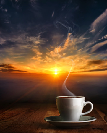 Coffee in white pottery cup on old wooden table with blurred image of  sunset or sunriseの写真素材