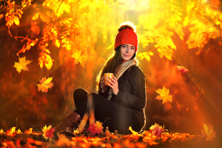 Beautiful girl drinking coffee on an autumn backgroundの写真素材