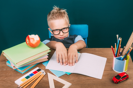 Funny school boy sitting on the desk with many school supplies.の写真素材