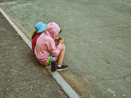 Two baby girls sitting on the side of the road and looking at a smartphone.の写真素材