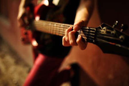 Man plaing guitar on sunset against urban wall