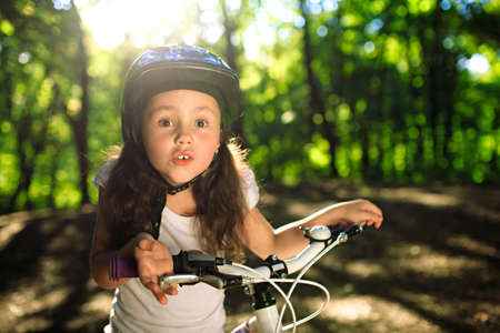 Portrait of a little girl on a bicycle in summer park outdoorsの写真素材
