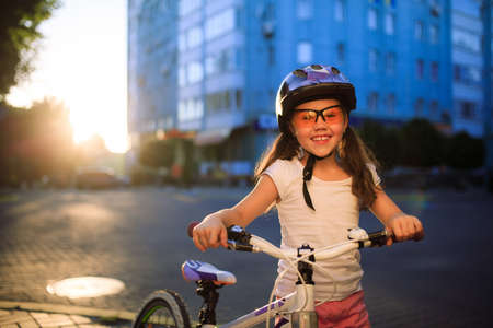 Portrait of a little girl on a bicycle in summer park against sunsetの写真素材