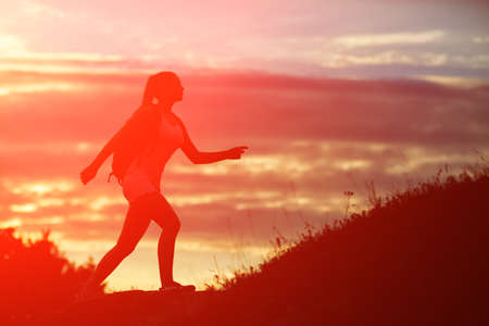 Happy sportswoman with red backpack walking on sunset summer.の写真素材
