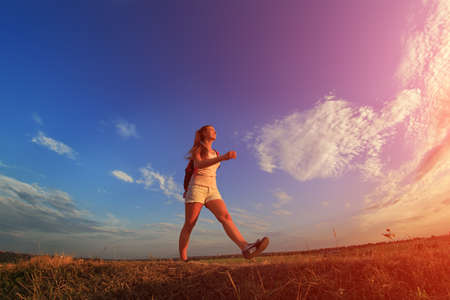Happy sportswoman with red backpack walking on sunset summer.の写真素材