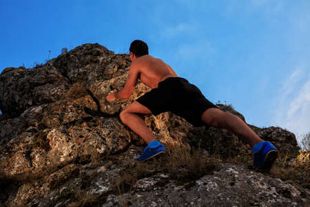 Muscular Climber climbs on a cliff with blue sky on backgroundの写真素材