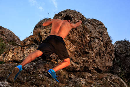 Muscular Climber climbs on a cliff with blue sky on backgroundの写真素材
