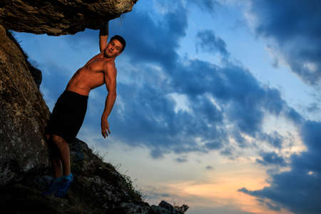 Muscular Climber climbs on a cliff with blue sky on backgroundの写真素材