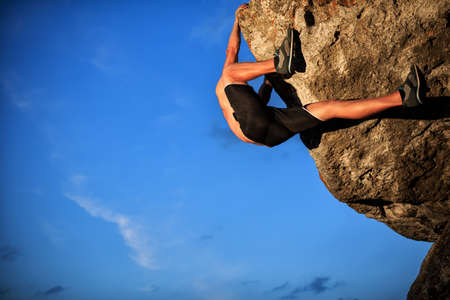 Muscular Climber climbs on a cliff with blue sky on backgroundの写真素材