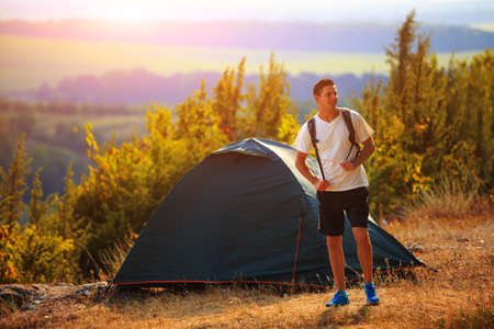 Men walk along the hill with backpack and with white clouds and mountains on backgroundの写真素材