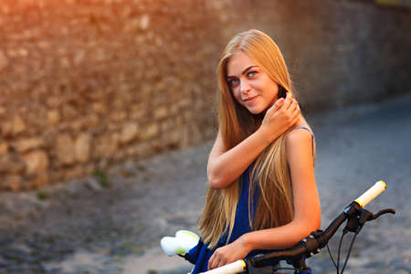 Young attractive girl in blue jeans shorts is posing on a bicycle near the wallの写真素材