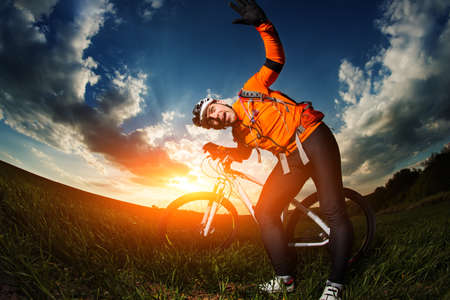Man Cyclist in Orange Jersey with bike on sunsetの写真素材