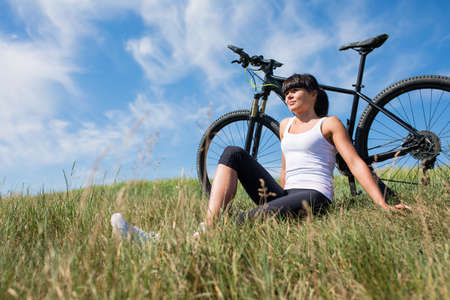 Mountain biking happy sportive girl in white shirt relax in meadows sunny countrysideの写真素材