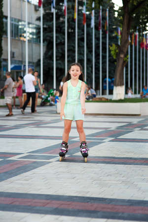 Little pretty girl rides on roller skates at a park on sunsetの写真素材