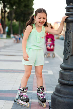 Little pretty girl rides on roller skates at a park on sunsetの写真素材