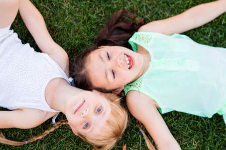 Two little sisters having fun in summer park while laying on lawn.の写真素材