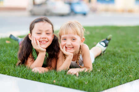 Two little sisters having fun in summer park while laying on lawn.の写真素材