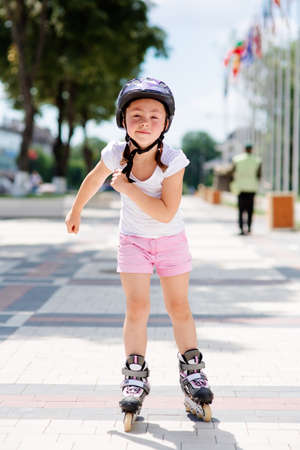 Little pretty girl on roller skates in helmet at a park. Front viewの写真素材