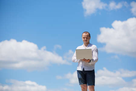 Man using his laptop computer against blue skyの写真素材