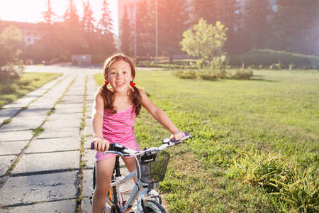 happy child girl riding bicycle in summer sunset in the park. Active kidsの写真素材