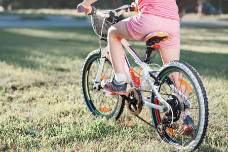 Little brunette girl in helmet riding bicycle in the park at sunset. back viewの写真素材