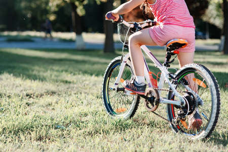 Little brunette girl in helmet riding bicycle in the park at sunset. back viewの写真素材