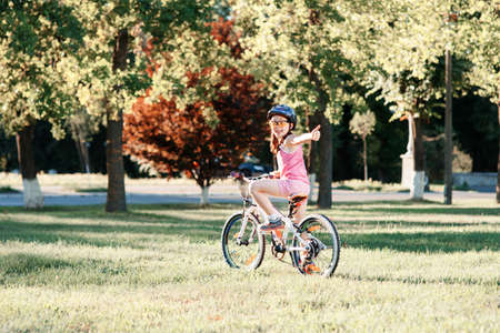 Little brunette girl in helmet riding bicycle in the park at sunset. back viewの写真素材