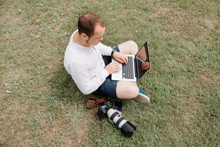 Young man photographer using laptop and camera in the park on a summers dayの写真素材