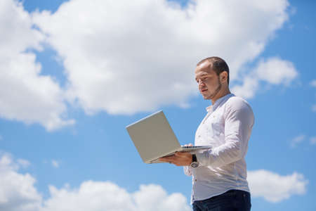 Happy business man looking to his laptop against blue sky