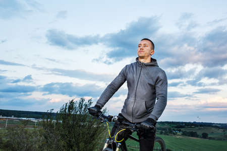 Young man cycling on a rural road through green spring meadow during sunsetの写真素材