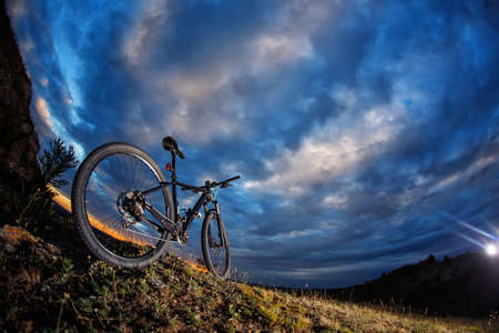 Mountain bike standing against cloudy sky against sunsetの写真素材