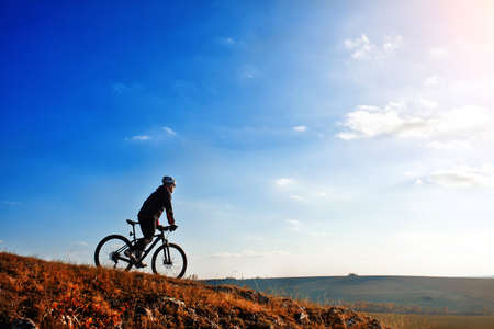 Cyclist riding his bike down on mountain trail. Beautiful sky and clouds on backgroundの写真素材