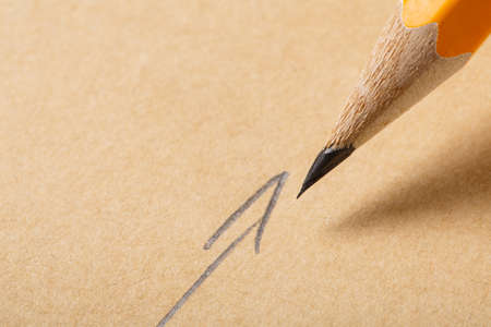 Holding a pencil on a brown paper background, Drawing with pencil for Sign of Arrow