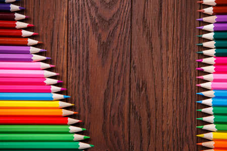 colored pencils on brown background lying in opposite sides of wooden tableの写真素材