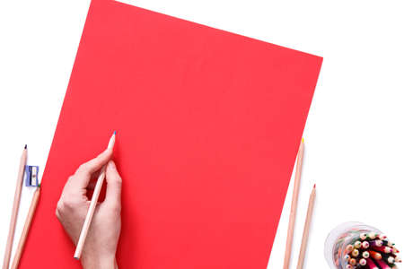 Female hand is ready for drawing with blue pencil on red paper. Isolated on white.の写真素材