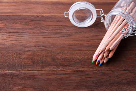 Set of coloured pencils in a glass pot on a wooden tableの写真素材